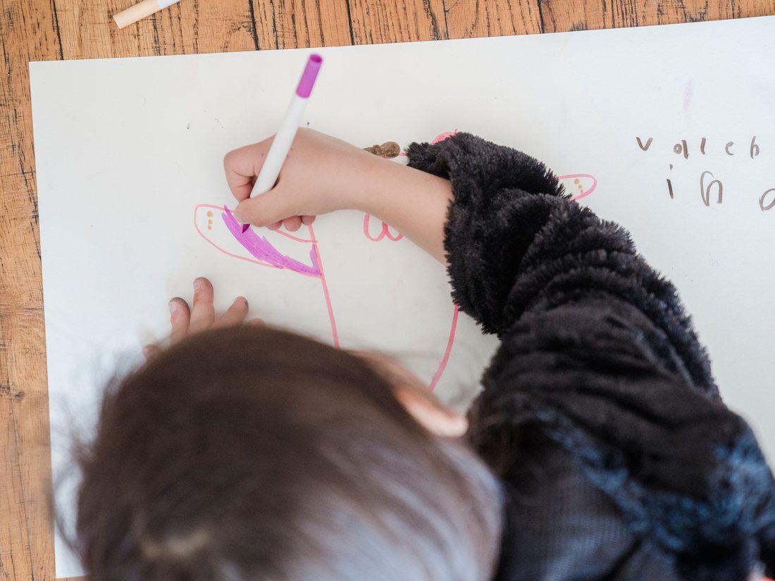 Un enfant qui dessine au feutre sur une grande feuille, vu du dessus; image d'ambiance