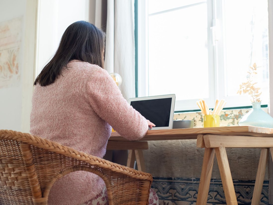 Une personne de dos devant son ordinateur portable, à sa fenêtre; image d'ambiance