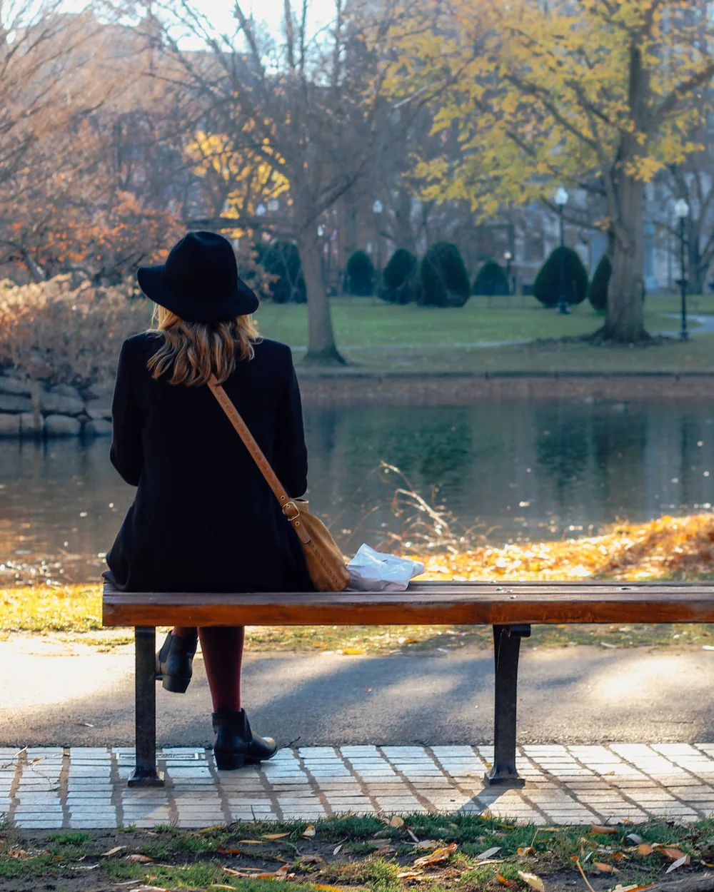 Une personne de dos, assise sur un banc devant l'eau, en automne; image d'ambiance