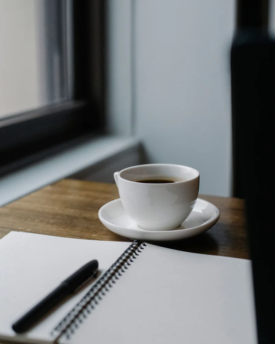 Un carnet ouvert, un stylo et une tasse près d'une fenêtre; image d'ambiance
